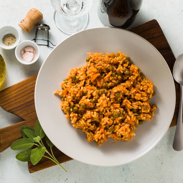 Italian risotto with tomato sauce and green peas, served in a plate on a wooden cutting board. classic Mediterranean cuisine. healthy vegan meal for the whole family - Photo, image