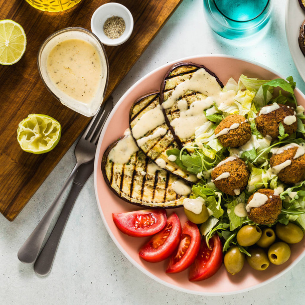 an appetizing dinner or lunch from a salad with tomatoes, grilled eggplants and legume falafel with sesame tahini dressing. Vegan healthy food for the whole family - Photo, Image
