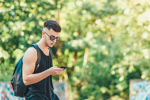 Handsome man checking mail on smartphone using application while spending time on city street, image of male in trendy outfit sending text messages via cellphone chatting in networks outdoors - Zdjęcie, obraz