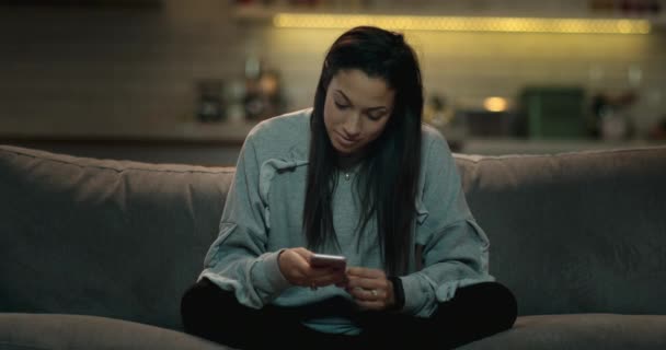 Woman sitting on a sofa in a cozy living texting her friends - Footage, Video