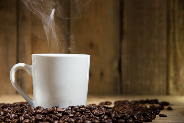 warm kopje koffie op de houten tafel en koffiebonen - Foto, afbeelding