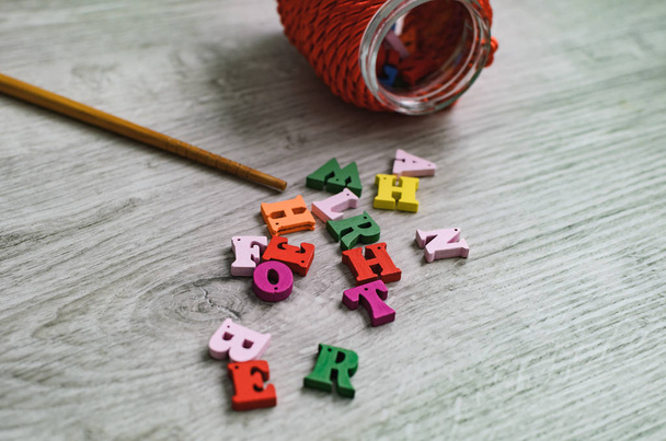 Lettere multicolori dell'alfabeto, contenitore per lettere e un puntatore scolastico in legno su sfondo di legno
. - Foto, immagini