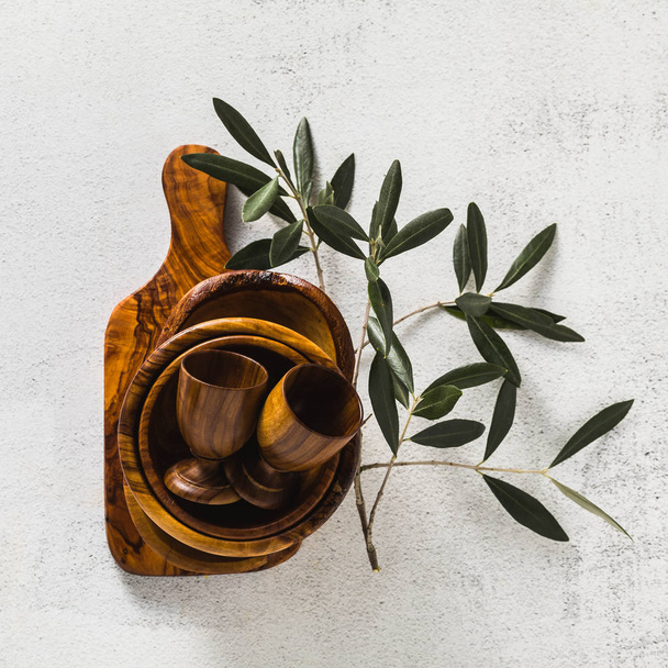 wooden utensils from the olive tree on the white kitchen table and the branches of the olive tree. eco-friendly kitchenware - Fotó, kép