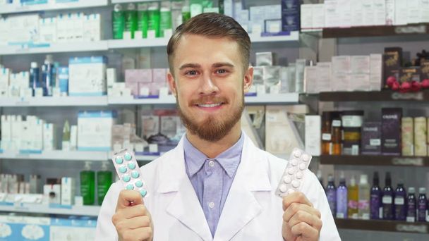 Joven farmacéutico mostrando medicación y sonriendo
 - Foto, Imagen