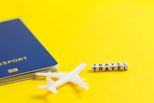 toy aircraft with blue passport on yellow paper background, travel concept, white block word TRAVEL. - Photo, Image