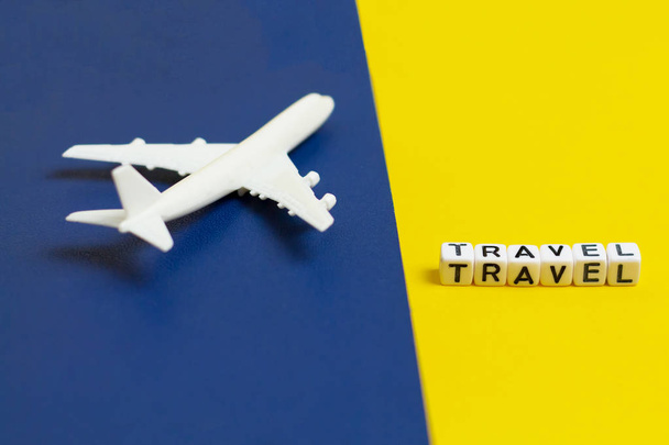 игрушечный самолет на сине-желтый цвет бумаги фона, концепция путешествия, белый блок слово TRAVEL
. - Фото, изображение