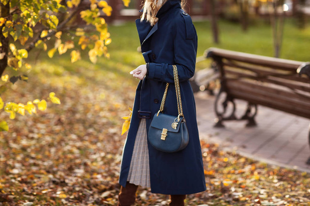 Красива модна жінка прогулюється по осінньому парку в синьому пальто з сумкою в руках. Подробиці
 - Фото, зображення