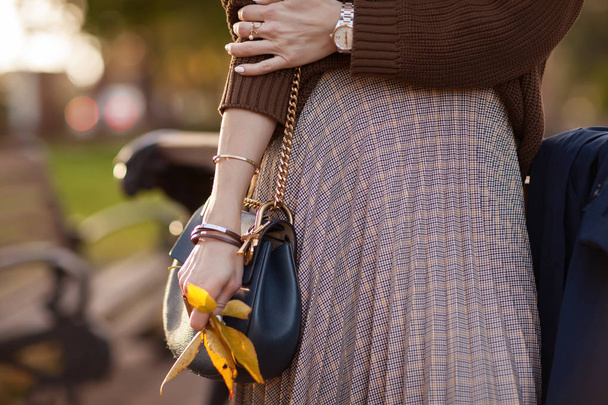 Krásná módní žena stojí v podzimním parku v hnědý svetr a dlouhá kostkovaná sukně s taškou v ruce. Podrobnosti - Fotografie, Obrázek