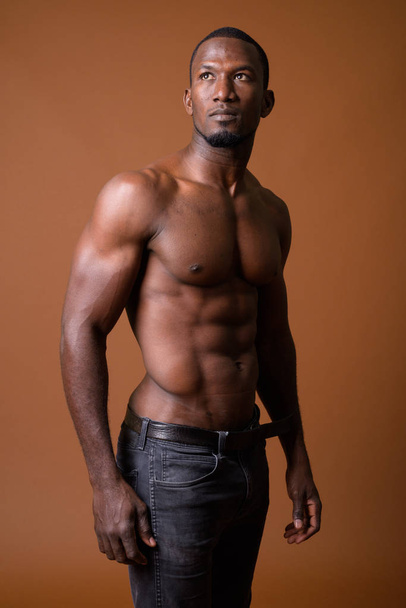 Handsome muscular African man shirtless against brown background - Fotoğraf, Görsel