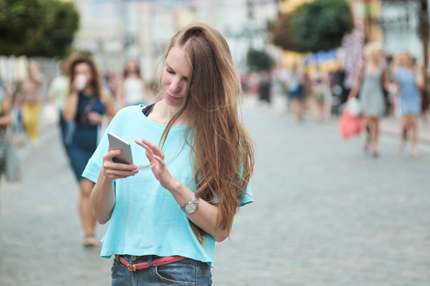 Молода худа руда дівчина гуляє по вулиці і друкує щось на своєму смартфоні
. - Фото, зображення