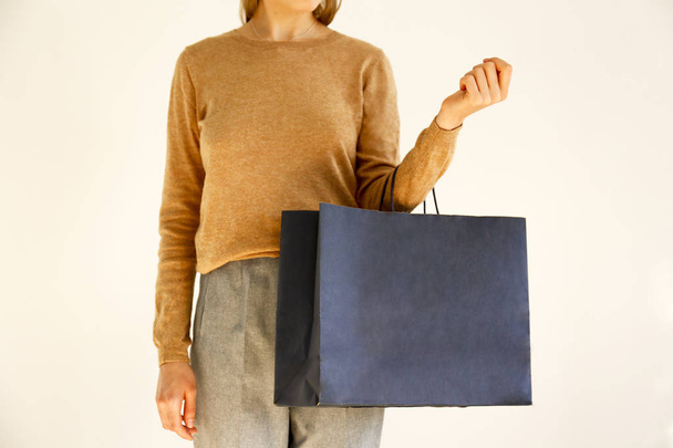 Young slim woman in classic fashionable outfit, brown sweater and loose grey pants, shopping, holding paper bags. White background, copy space, close up. Black friday sale concept. - Foto, immagini