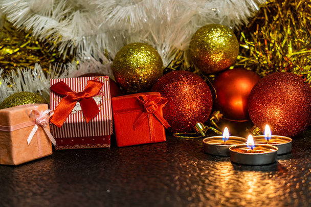 Christmas and new year's composition of red balls for Christmas trees and Golden tinsel, in the light of candles on a dark background with space for text. Holiday gifts, surprises. Winter cones and ornaments in beautiful lights. - Photo, Image