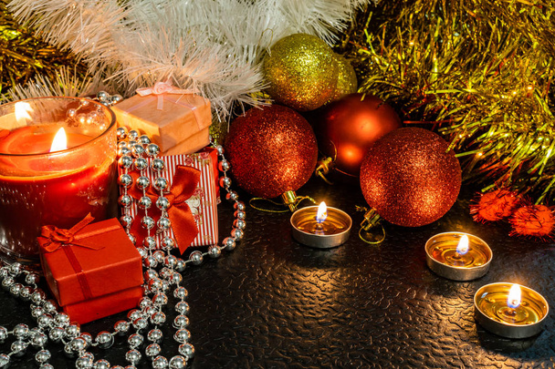 Navidad y la composición de año nuevo de bolas rojas para los árboles de Navidad y oropel de oro, a la luz de las velas sobre un fondo oscuro con espacio para el texto. Regalos navideños, sorpresas. Conos de invierno y adornos en hermosas luces
. - Foto, imagen