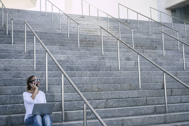 businesswoman using computer and using smartphone while sitting on stairs  - Photo, Image
