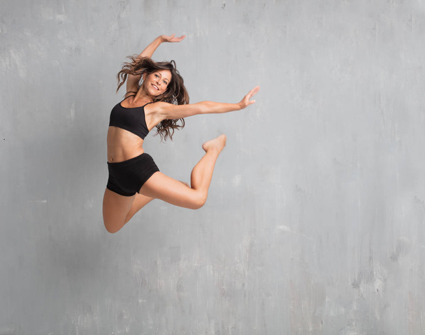 young pretty woman street dancer jumping against grunge wall background - Фото, изображение