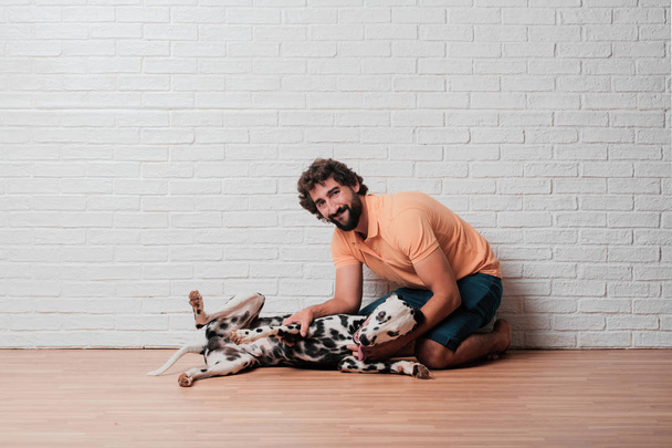 young bearded man with a dalmatian dog against white brick wall background - Fotó, kép
