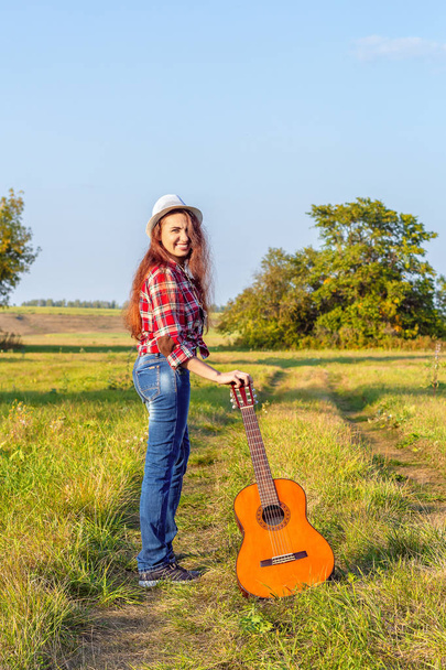 Yaz aylarında bir gitar güzel, mutlu, Kızıl saçlı kız günbatımı bir arka plan üzerinde bir alanda. Yaratıcı özgürlük kavramı - Fotoğraf, Görsel