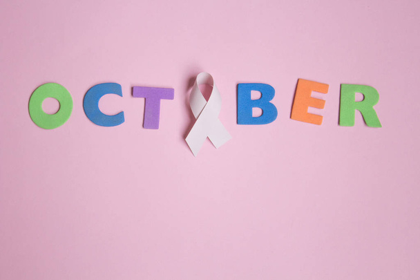 Word October with Pink ribbon symbolic bow color for Breast cancer awareness on pink background - Fotó, kép