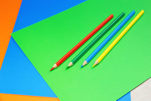 Colorful pencils and sheets of paper on white wooden desk and dark blue background - Foto, afbeelding