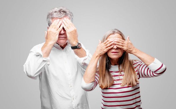 senior cool husband and wife with a serious, scared, frightened expression, covering eyes with both hands. - Photo, image
