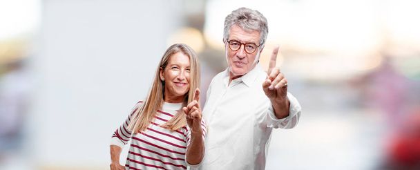senior cool husband and wife smiling and looking satisfied and happy, counting number with one finger. - Foto, Bild