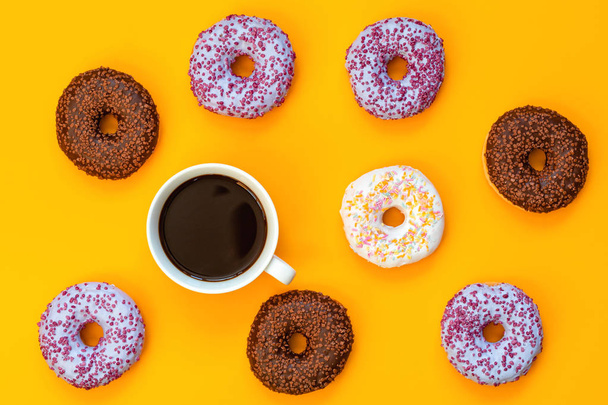 Delicious glazed donuts and cup of coffee on yellow surface. Flat lay minimalist food art background. Top view. - Фото, изображение