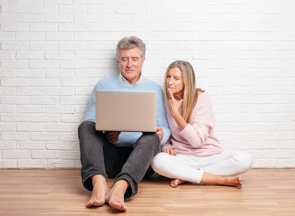 pretty senior couple sitting on their house floor with a laptop - Photo, Image