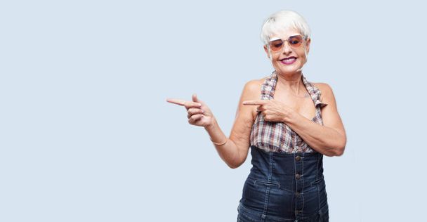 Senior cool Frau lächelt und zeigt zur Seite mit beiden Händen, in Richtung der Stelle, wo der Publizist ein Konzept zeigen kann. - Foto, Bild