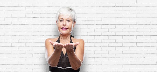 senior cool woman smiling with a satisfied expression showing an object or concept with both hands, pointing both of them forward. - Foto, imagen