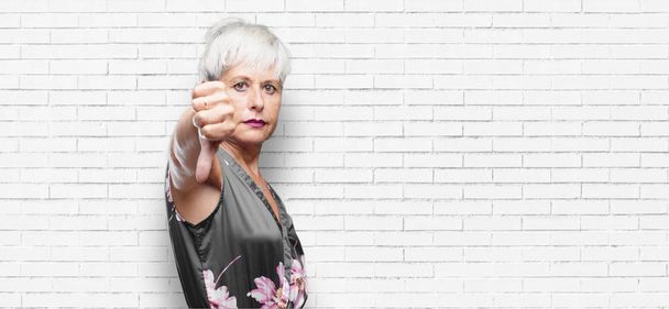senior cool woman with a dissenting, serious, stern expression, with thumbs down in disapproval. - Fotoğraf, Görsel