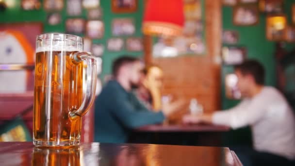 Guy friends drinking beer and discuss something on the background. Pint of beer in focus - Footage, Video