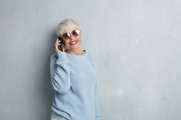 senior cool woman with a smartphone against grunge cement wall. - 写真・画像