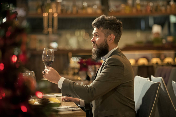 Spending great time in restaurant. Handsome young man holding glass with red wine and smiling at the restaurant. - Photo, Image