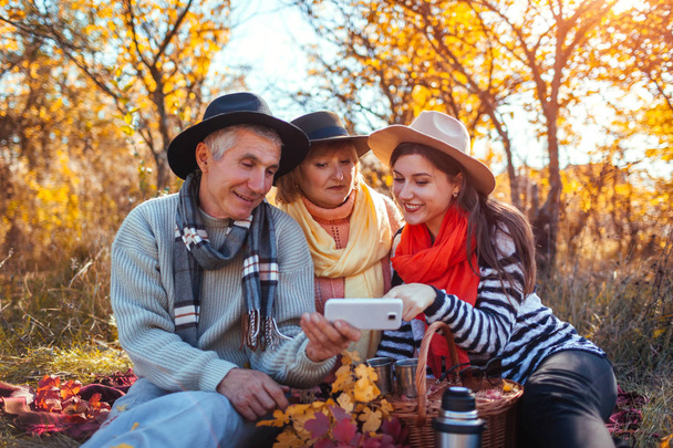 シニアの親娘秋の森でスマート フォンを使用して。家族の価値観。一緒にピクニックを持つ人々 - 写真・画像