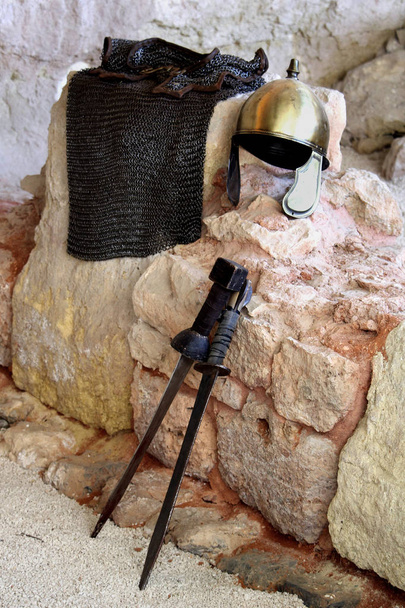 Roma pirinç kask, zırhlı tunik ve taş duvara yaslanmış iki kısa kılıç - Fotoğraf, Görsel