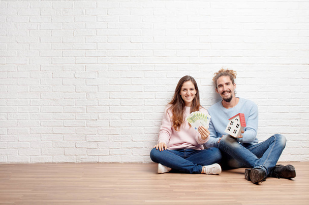 Happy young couple sitting on the floor of their new house. Concept of love and moving house. - Fotó, kép