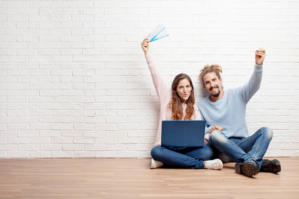 Happy young couple sitting on the floor of their new house with a laptop buying a boarding tickets. Travel concept. - 写真・画像