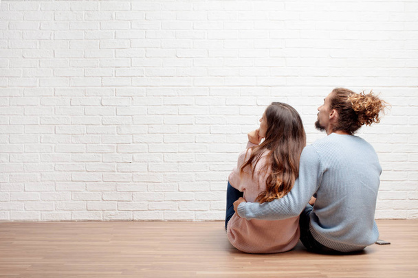 Happy young couple sitting on the floor of their new house. Concept of love and moving house. - Fotó, kép