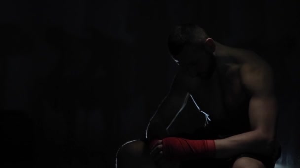 Ein besorgter, gut aussehender männlicher Athlet mit gesenktem Kopf sitzt in der Dunkelheit. Lichtspiel. Ein verzweifelter Boxer - Filmmaterial, Video