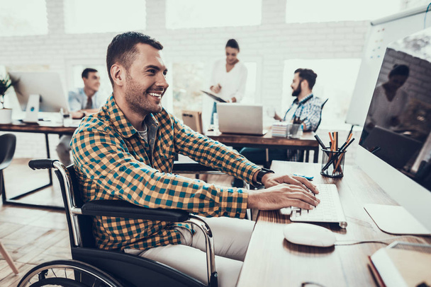 Man on Wheelchair Working on Computer in Office. Disabled Young Man. Man on Wheelchair. Recovery and Healthcare Concepts. Teamwork in Office. Young Worker. Sitting Man. Working Man. - 写真・画像