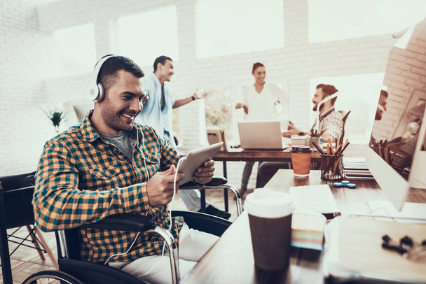 Young Man on Wheelchair with Headphones in Office. Disabled Young Man. Man on Wheelchair. Recovery and Healthcare Concepts. Listen to Music. Young Worker. Sitting Man. Man with Digital Device. - Foto, afbeelding