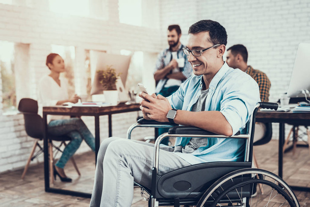 Man in Glasses on Wheelchair with Phone in Office. Talking on Phone. Disabled Young Man. Man on Wheelchair. Recovery and Healthcare Concepts. Teamwork in Office. Young Worker. Sitting Man. - Zdjęcie, obraz