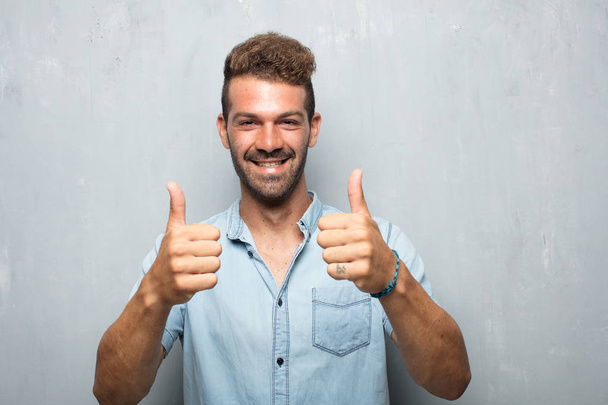young handsome man with a satisfied, proud and happy look with thumbs up, signaling OK with both hands, sending a positive, "alright' message. - Foto, Bild