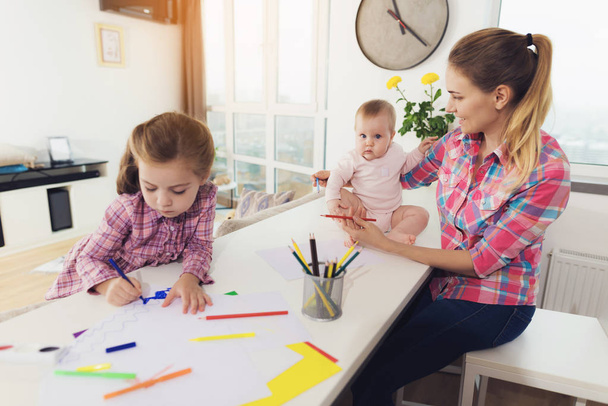 Girl Painting with Mother and Younger Sister. Cute Pretty Child Drawing on Paper with Colored Pencils at White Table. Younger Baby Looking at Sisters Picture. Children Activity Concept - Фото, изображение