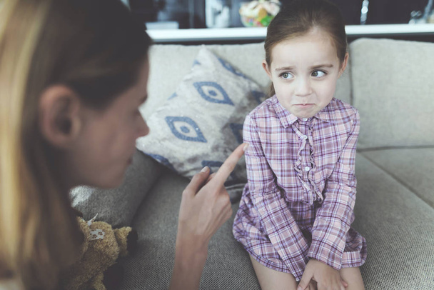 Young Mother Scolding Upset Pretty Child Indoors. Caucasian Girl Sitting on Comfortable Couch in Modern Living Room Feels Guilty and Looking at Swearing Mother. Family Relationship Concept - Photo, Image