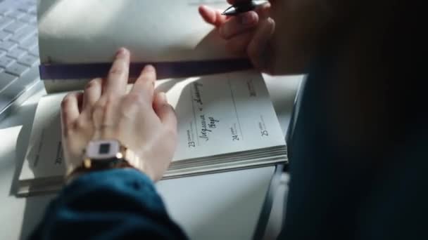 eine Nahaufnahme eines Mädchens, das eine Notiz in ihr Notizbuch schreibt, das auf einem weißen Tisch neben einer weißen Tastatur liegt - Filmmaterial, Video