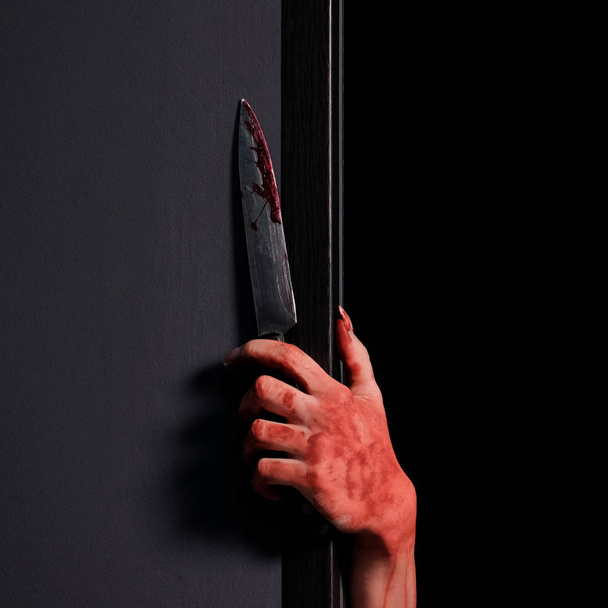 Female hand looks out from behind the wall with a bloody knife.Halloween celebration concept. Close-up. Square picture frame. Black background. - Fotó, kép