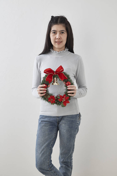 Πορτραίτο της ομορφιάς νεαρής γυναίκας με Χριστουγεννιάτικο στεφάνι και δώρο σε φόντο λευκό τοίχο - Φωτογραφία, εικόνα