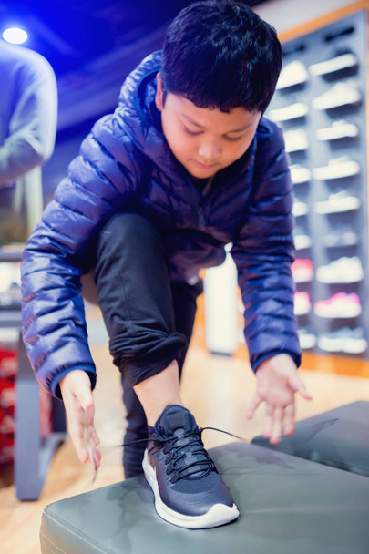 Selective focus to asian boy stand and tying sport shoelaces in sport shop before test size and buy it. - Фото, изображение