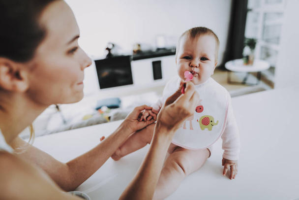 Happy Mom Feeds Adorable Baby with Spoon Indoors. Mother Diving Healthy Food to Cute Hungry Toddler In Bright Living Room. Happy Family Having Breakfast in Kitchen. Motherhood and Childhood Concept - Foto, imagen